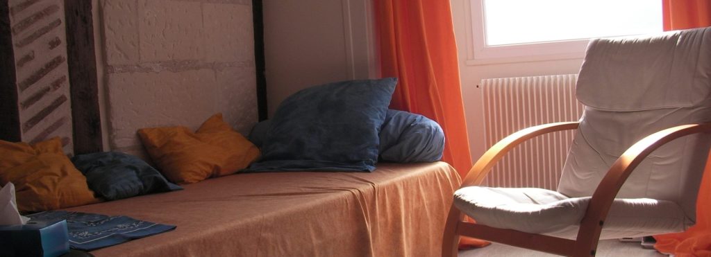 Un adolescent en sweat à capuche participe à une séance de thérapie avec une thérapeute, assis sur un canapé.